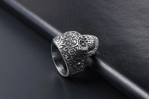 Macro view of gothic skull ring with floral carvings on black leather background