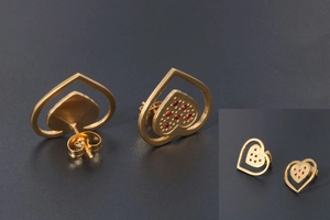 Detail of gold-plated titanium heart earrings with hollow frame and red crystal inlay