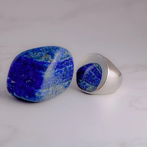 Polished men's signet ring with round blue lapis lazuli stone on white marble