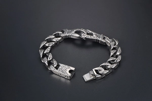 Macro detail of silver punk Cuban link bracelet with engraved religious symbols