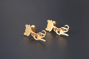 Close-up of golden cat stud earrings with red rhinestone accents and matte finish