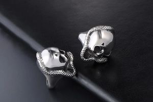 Close-up of gothic stainless steel skull and snake rings on black leather background