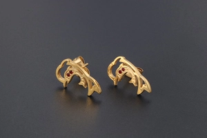 Detail shot of golden dolphin stud earrings with red crystal eyes and hollow design
