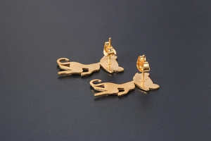 Close-up of golden cat stud earrings with brushed texture on a grey surface