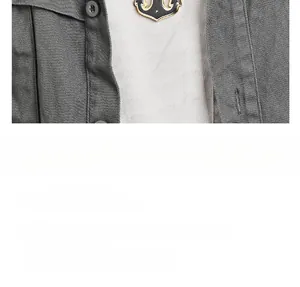 Détail d'un pendentif ancre marin noir et or porté sur une chemise en jean grise