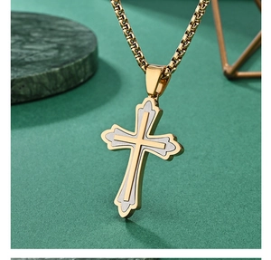 Détail macro d'un pendentif croix en acier bicolore sur une chaîne box dorée fine