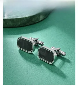 Detail view of silver cufflinks with black textured inlay on a green marble background