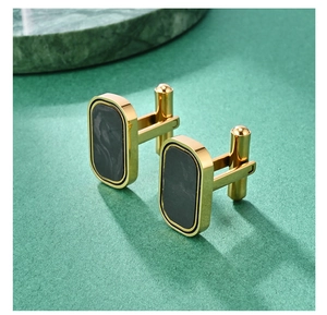Macro shot of rectangular gold cufflinks with black marble inlay on a green surface