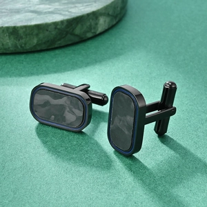 Minimalist black carbon fiber cufflinks with grey texture and blue trim on green surface