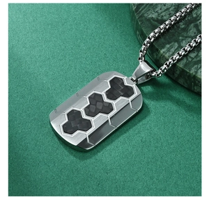 Close-up of brushed steel pendant with black carbon fiber inlays on dark textured surface