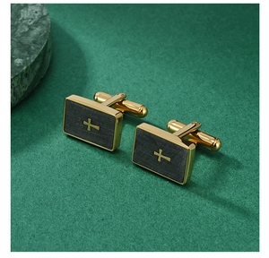 Detail of gold and grey brushed metal cufflinks with a cross motif on green marble surface