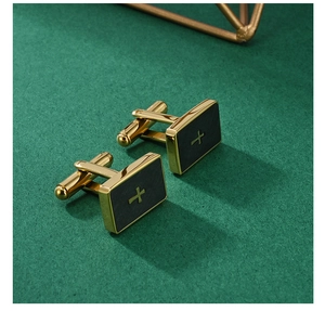 Detail of gold and black men's cufflinks with cross pattern on dark green background