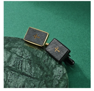 Close-up of dual-tone cufflinks with brushed grey finish and golden cross on marble surface
