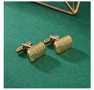 Detail goldener Manschettenknöpfe mit Krokoprägung, gebürstetem Metall und kleinem Kristall