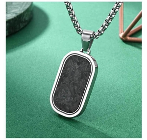 Detail of oval carbon fiber pendant and silver box chain on a green background