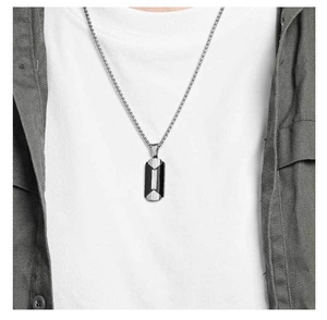 Close-up of dual-tone rectangular pendant necklace worn over white t-shirt and grey jacket