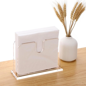 Clear acrylic cocktail napkin holder on a light wood table with elegant boho decor
