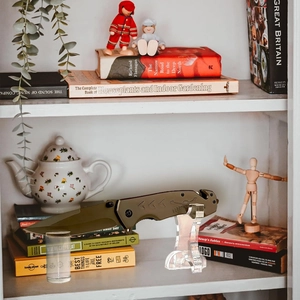 Tactical folding knife with olive green handle on clear acrylic display stand for home decor