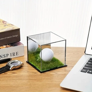 Close-up of clear acrylic golf ball display case with green turf base on an office desk