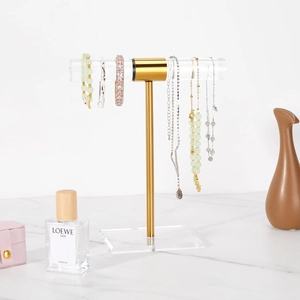 Close-up of golden T-bar jewelry display stand with acrylic base on marble surface