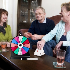 Three adults playing a poker game with a 12-inch 12-slot colorful prize wheel in a living room