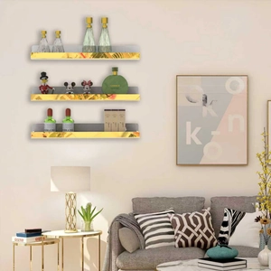 Three-tier gold acrylic floating shelves on wall displaying perfume and decor items