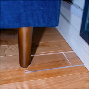 Close-up of clear acrylic furniture stopper installed under blue sofa leg on wood floor