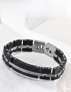 Détail du bracelet pour homme en acier noir mat et argent sur fond de marbre blanc