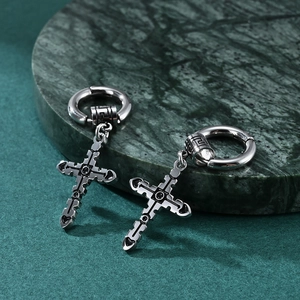 Gothic stainless steel hoop earrings with engraved cross pendants on a green marble base