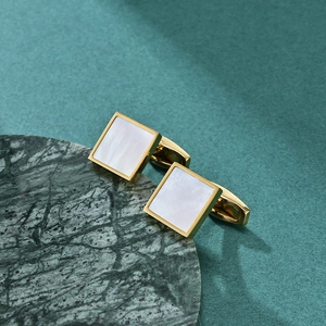 Square gold cufflinks with white mother of pearl inlay on green marble surface