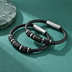Braided leather bracelet with dual-tone metal charms and magnetic clasp on marble base
