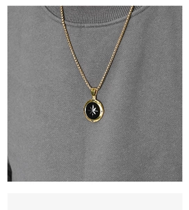 Dettaglio della collana a bussola da uomo con catena box dorata su maglia grigia