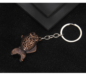 Detailed view of a vintage bronze hollow carp keychain on a textured black background