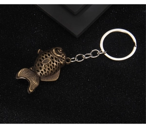 Detail of vintage bronze fish keychain with hollow design on black textured background