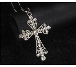 Macro shot of silver-colored hollowed cross pendant with crystal inlay on black texture