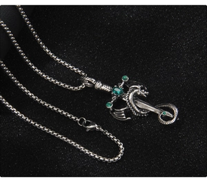 Detailed view of vintage silver dragon wrapped around a sword pendant with green crystals