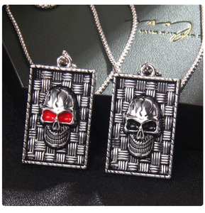 Detail of retro punk skull tag pendant featuring red eyes and woven metal texture