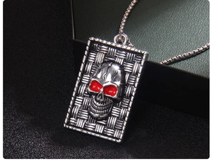 Macro shot of silver gothic skull pendant with red eyes on a long box chain necklace