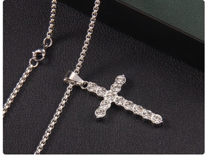 Macro shot of silver box chain and cross pendant with inlaid clear crystals on black texture