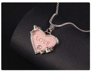 Detail eines rosa glitzernden Herzanhängers mit LOVE-Text und kleinem Kristall an einer Kette