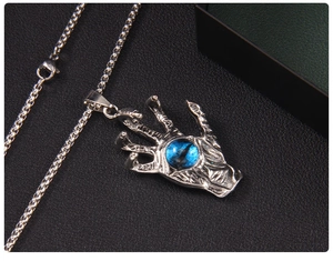 Detailed view of silver punk claw pendant with blue evil eye on black textured surface