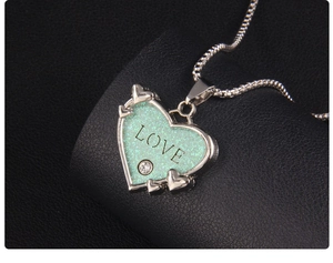 Detail eines silbernen Herzanhängers mit grünem Glitzer, LOVE-Text und klarem Straßstein
