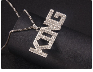 Detailed view of silver KING letter pendant with micro-paved rhinestones on a black stand