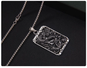 Detailed relief of a silver dragon emblem on a rectangular stainless steel pendant