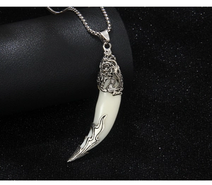 Détail du pendentif en forme de croc avec gravure de dragon sur une chaîne à billes argentée