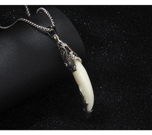Détail macro du pendentif dent de loup avec calotte en métal gravé et chaîne en acier