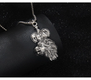 Detailed close-up of antique silver lion head pendant with crown on black display stand