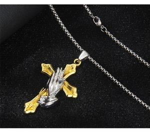 Macro detail of gold cross and silver praying hands pendant on a stainless steel chain