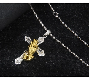 Detailed view of silver cross pendant with golden praying hands and steel box chain
