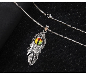 Détail d'un pendentif plume argentée avec œil de démon sur fond noir texturé